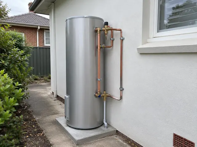 Outdoor hot water cylinder with copper pipework beside a rendered house wall in Eastwood