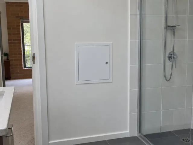 Bathroom wall with a small access panel beside a tiled shower and dry wall in Macquarie Park